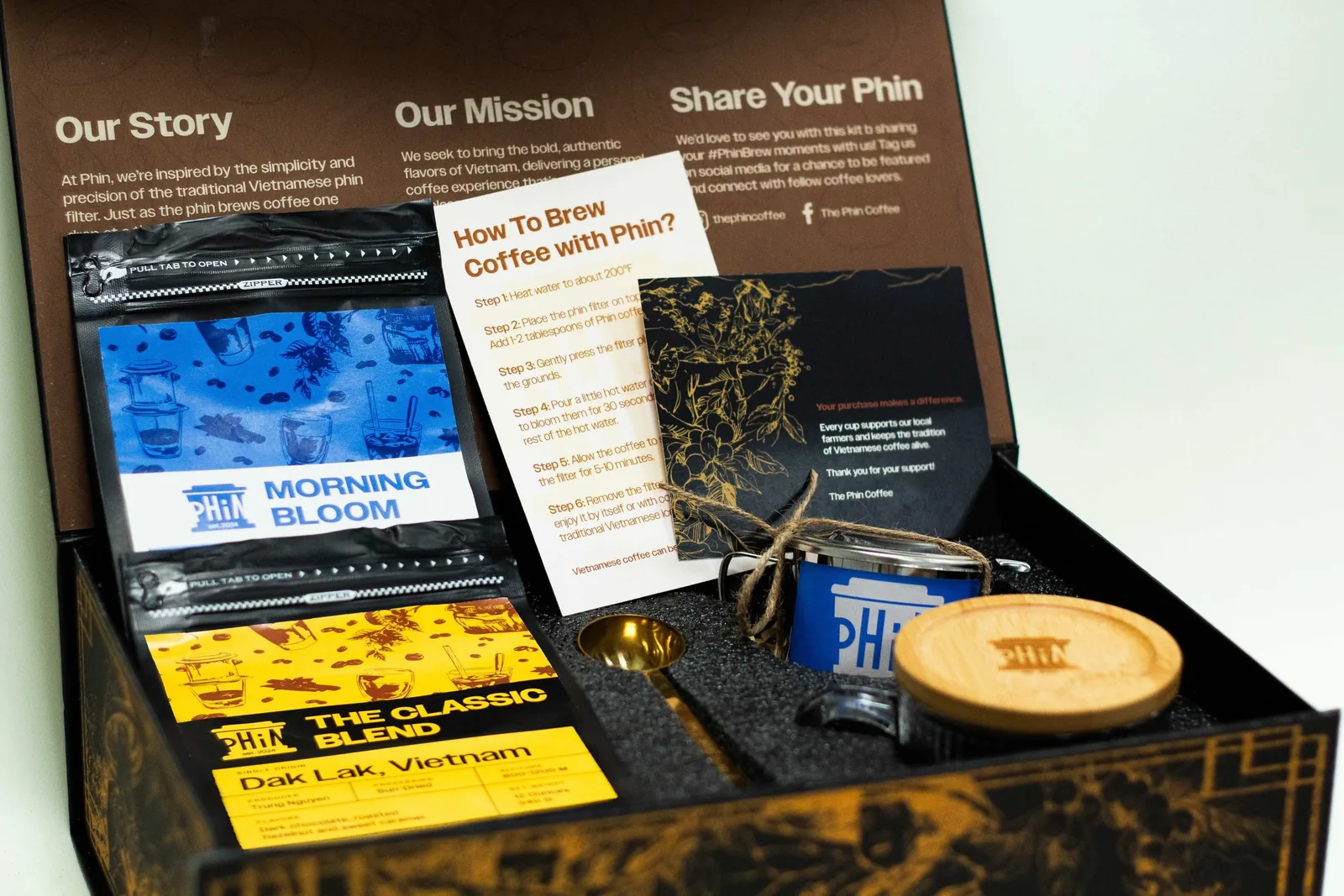 Open Phin gift box with two coffee bags, a phin filter, glass mug and brew guide